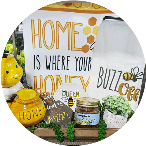 A collection of bee-themed home decor and gifts, including a Home is Where the Honey is flag, bee with honey pot statue, buzz coasters, midwest honey, and a buzz off kitchen towel.